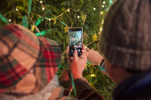 Two people holding their phone up to a gold star hanging on a Christmas tree and taking photos 