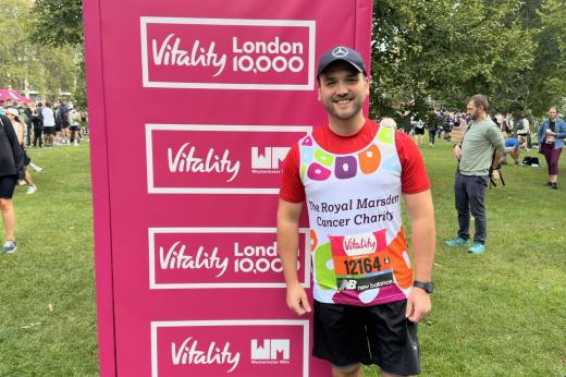 Team Marsden runner posing in front of a Vitality 10K sign in a busy London park