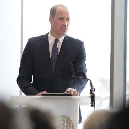 His Royal Highness Prince William smartly dressed in suit and tie standing at a podium and giving a speech