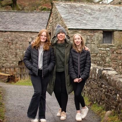 Royal Marsden patient Julie, standing with her two young daughters in coats and hats in front of old country buildings and dry stone walls.