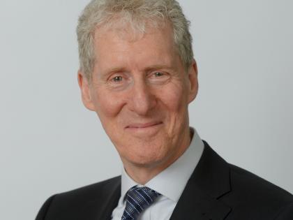 Portrait photo of Roger Gray. He is smiling and wearing a suit and tie. 