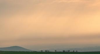 RMCC trekkers hiking in the distance with the sun shining on them and hills in the background