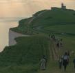 RMCC trekkers hiking over the south downs with the sun shining on them and the sea and cliffs in the background