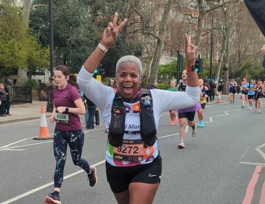 A Team Marsden runner smiles at the camera and raises two hands in the air.