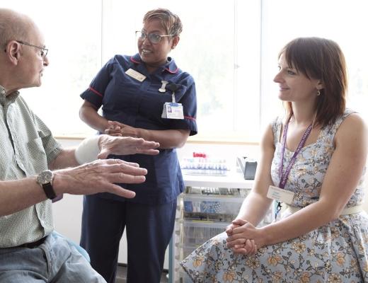 A patient sitting in a hospital room talking to two healthcare professionals who are smiling and listening to them intently