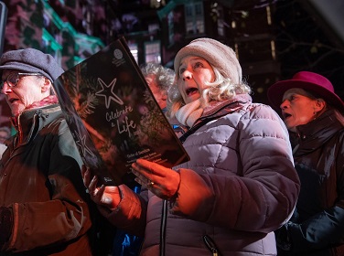 People wrapped up warm in coats and hats singing and holding a carol order of service booklet