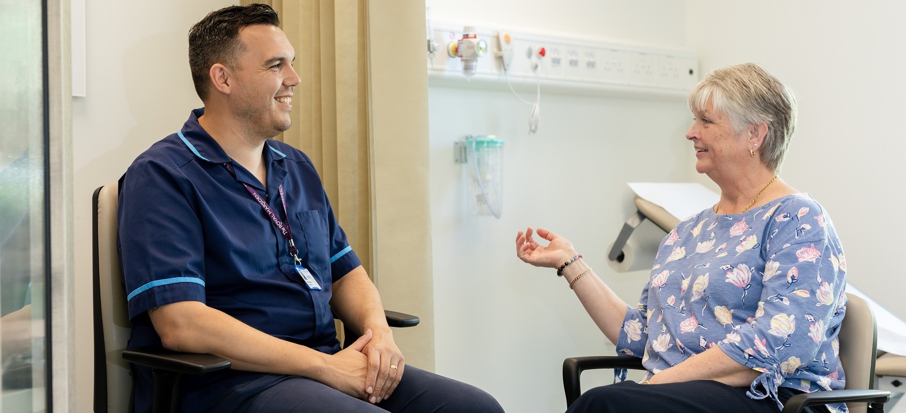 A Royal Marsden nurse sitting down and smiling and talking with a patient in a hospital room