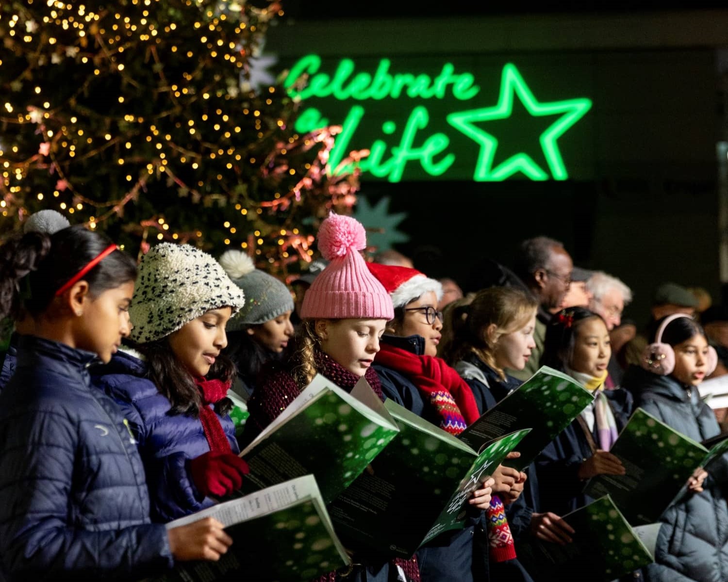 Children's choir singing in from of a lit Christmas tree 