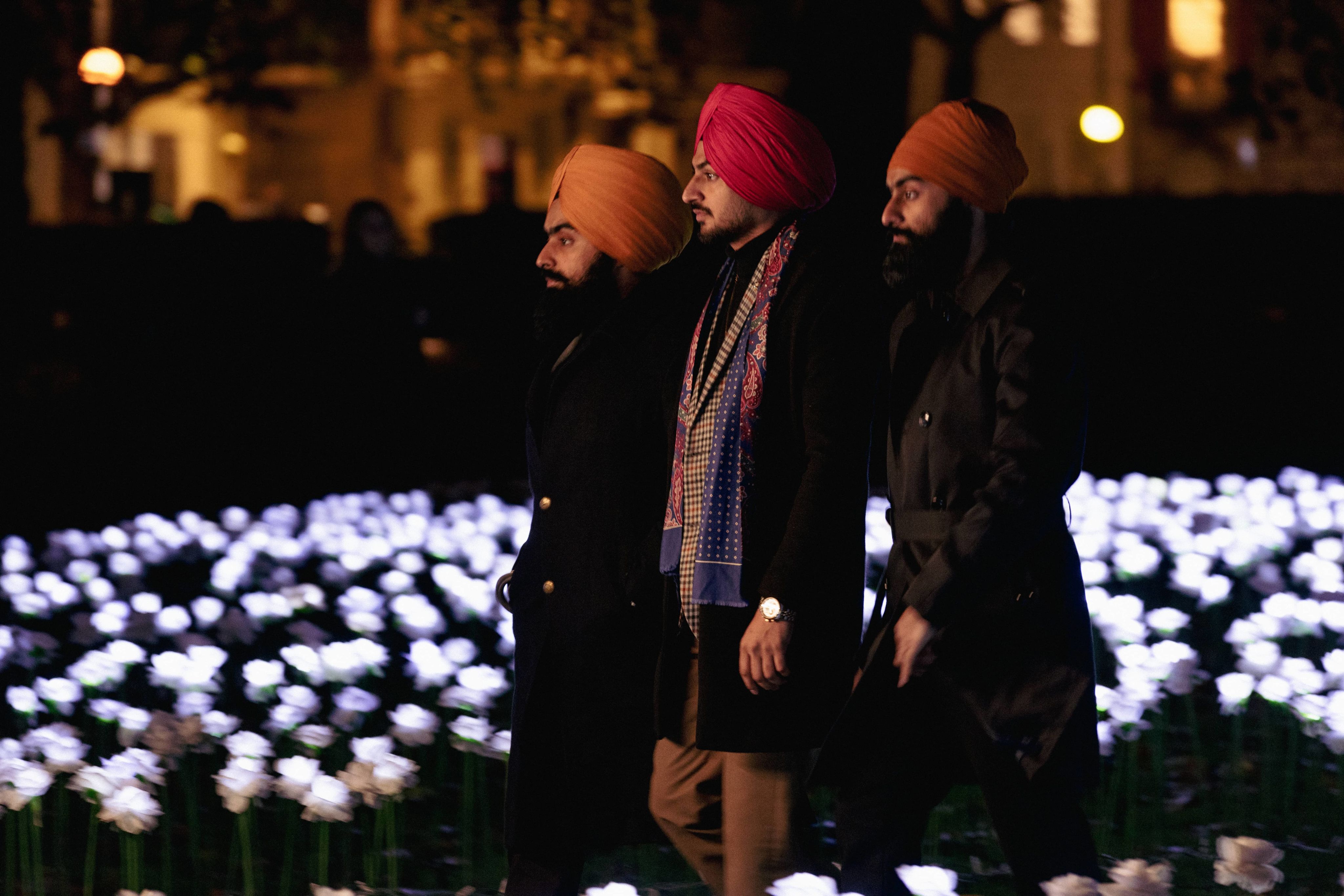 Three young men walking through the Ever After Garden. They are wearing dark coats an brightly coloured turbans.