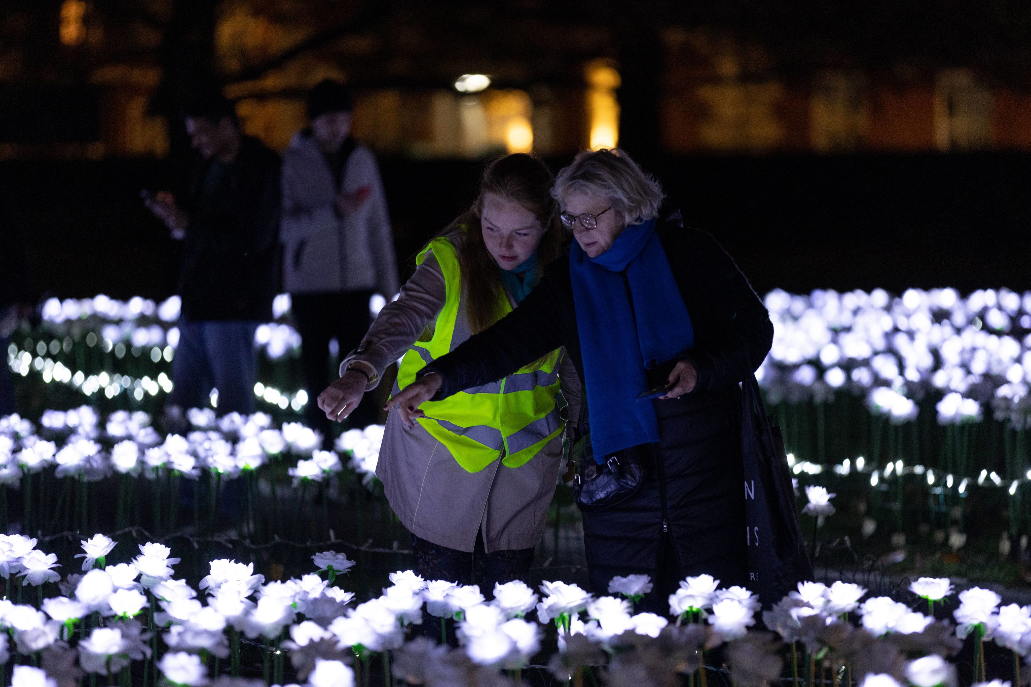 A volunteer wearing a high-vis jacket helping a woman in a blue scarf. They are both pointing toward the roses in the Ever After Garden