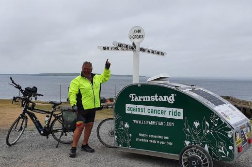 Simon Aylett poses at John O'Groats sign with his e-bike and mini caravan