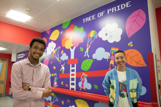 artist Ashton Attzs standing with Royal Marsden Youth Forum Member Joshua in front of the commissioned Tree of Pride inclusive mural