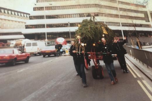 Four members of the London Fire Brigade pushing the tree along the street