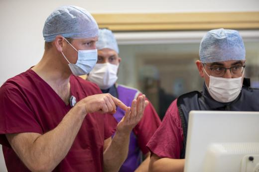 3 men talking and looking at computer screen, wearing surgical scrubs