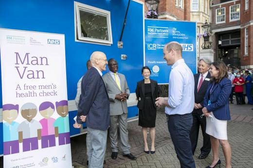 Group of people stood talking outside a van.  One of the men is HRH The Duke of Cambridge