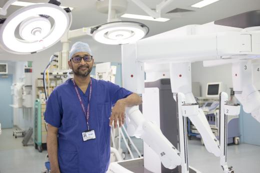 Professor Vinidh Paleri with the Da Vinci Xi robot. He is wearing blue scrubs and a cap. 