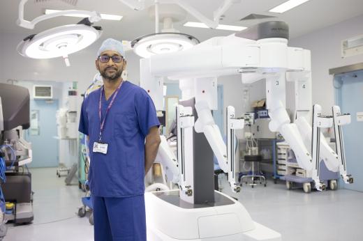 Professor Vinidh Paleri, wearing blue scrubs, standing in an operating theatre with the Da Vinci Xi Robot