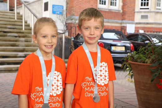 Reece and Emilie outside The Royal Marsden hospital in Chelsea. They are smiling, wearing orange charity branded t-shirts and have medals