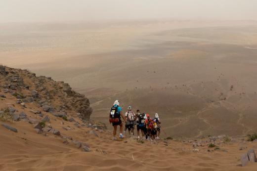 A landscape photo of a group of runners going down a huge rocky sand dune. 