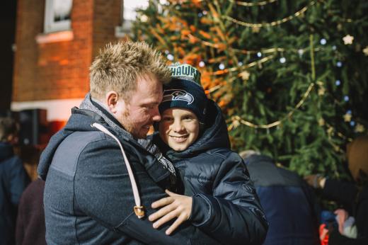 Photo of a man hugging his sun in front of the Celebrate a Life Christmas tree. They are wearing winter coats and smiling. 