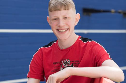 Photo of Ryan with a big smile. He is wearing a red and black shirt and has blonde hair