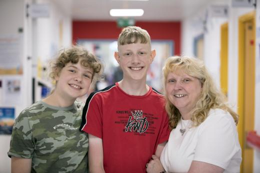 Ryan standing between his younger sister (left) and his mum Paula (right) all have big smiles and blonde hair.