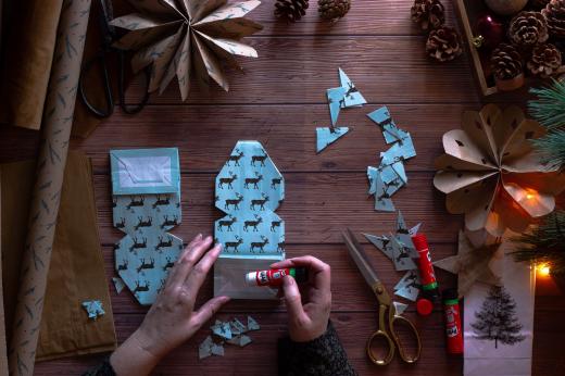 A top down angle photo of pair of hands making a Christmas craft paper snowflake. 