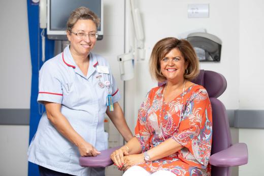 Louise and Senior Nurse Pilar in The West Wing. Louise is sat next to the Nurse in a purple treatment chair. She is wearing a bright orange and pink patterned shirt and both are smiling.