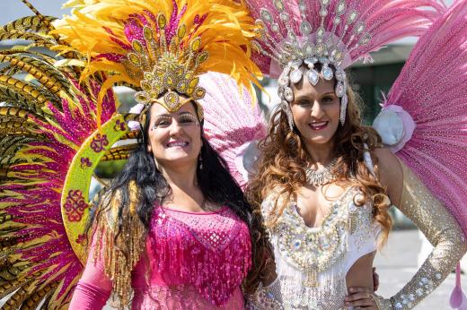 A pair of smiling performers in extravagant pink and silver samba dance outfits, covered in feathers and sequins.
