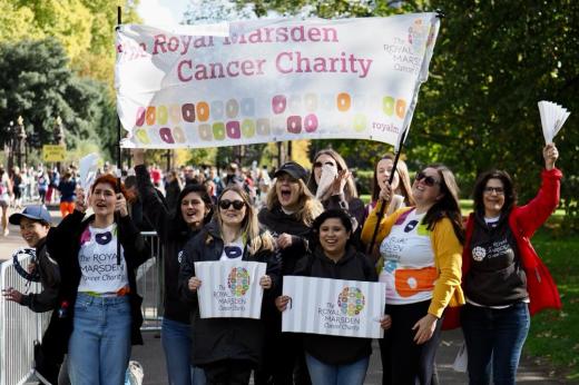 A group of volunteers at the Royal Marsden Cancer Charity cheer point wave banners and flags and smile at the camera