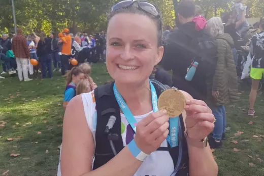 A Team Marsden runner, Kayleigh, smiles at the camera holding up her Royal Parks Half Marathon 2022 medal