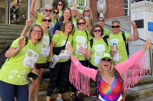 A group of people in green Banham Marsden March t-shirts, including someone in a colourful leotard with arm tassels at the front. They are standing on The Royal Marsden Chelsea steps.