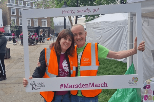 Two people in high visibility jackets smiling through a large Banham Marsden March picture frame