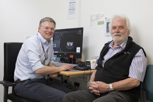 A doctor and patient sitting sitting in a hospital waiting room in front of a computer with an image of a medical scan on it