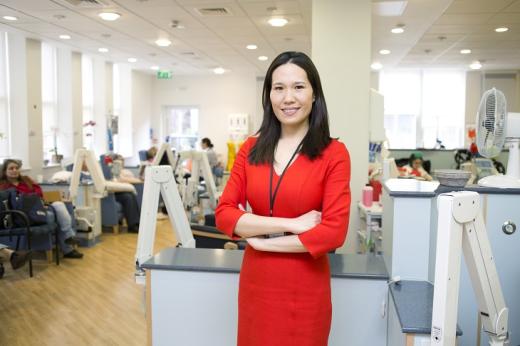 Dr Chong in a smart red dress standing with her arms crossed in a busy hospital setting