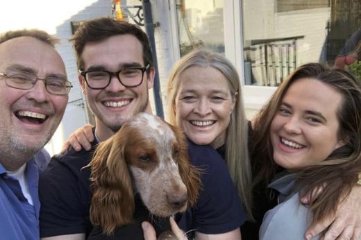 A family of four smiling in the garden and holding a brown and white dog