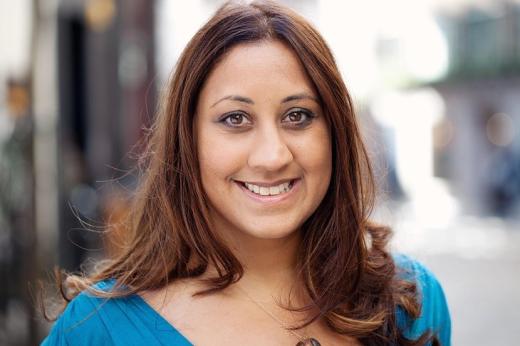  Header and shoulders of Toral, who is smiling and wearing a bright blue top and a gem stone necklace