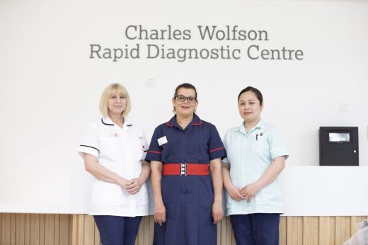 Three clinical staff members with the entrance to the Charles Wolfson Rapid Diagnostic Centre