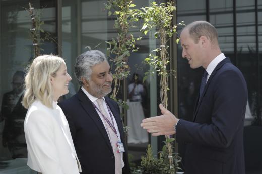 His Royal Highness Prince William speaking with Emma, a young woman wearing a white suit jacket and wavy blonde hair. Also with them is Emma's consultant from The Royal Marsden. He is wearing a dark suit and smiling.