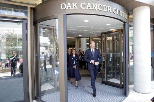His Royal Highness Prince William dressed smartly in a suit walking out of large glass sliding doors of the Oak Cancer Centre 