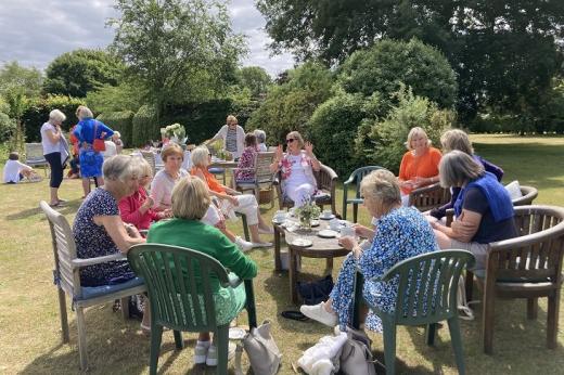 A group of people sitting on chairs in a lovely green garden on a warm summer's day