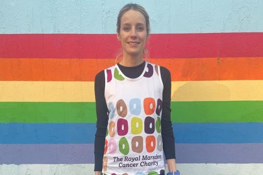 A woman in a Royal Marsden Cancer Charity running vest standing in front of a rainbow coloured wall