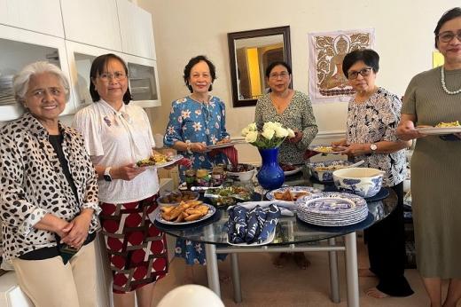 A group of women holding plates and gathered around a table with a selection of food