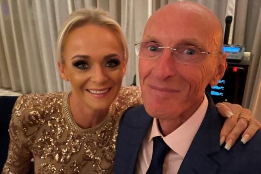 A woman in a gold and shiny dress with her hand around a man with a suit on, smiling