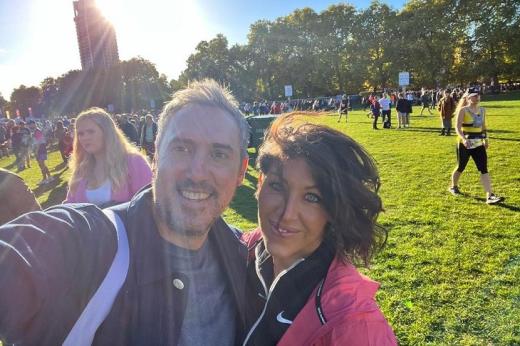 Two people standing together and smiling in a busy park