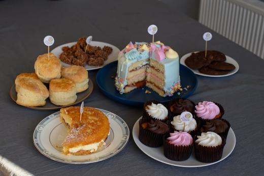 A selection of colourful cakes, cupcakes, biscuits and scones on a table with Royal Marsden Cancer Charity labels on each plate
