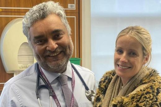 Emma in a fluffy coat and scarf standing next to a professor in a shirt and tie with a Royal Marsden badge and stethoscope around his neck