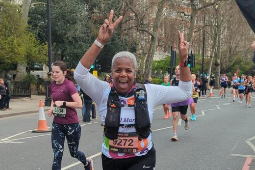 A Team Marsden runner smiles at the camera and raises two hands in the air.