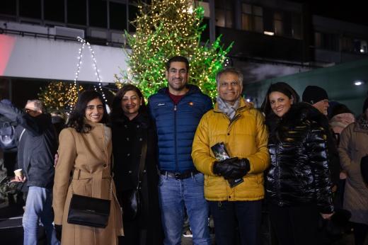 A family of five wrapped up warm in coats, standing in front of a large Christmas tree