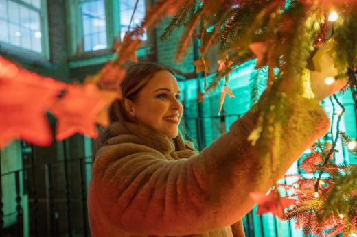 A person in a warm fluffy coat smiling and looking at a star on the Christmas tree